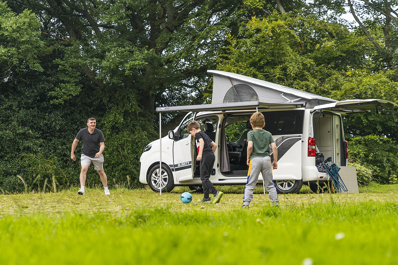 Family playing outside their campervan at the park
